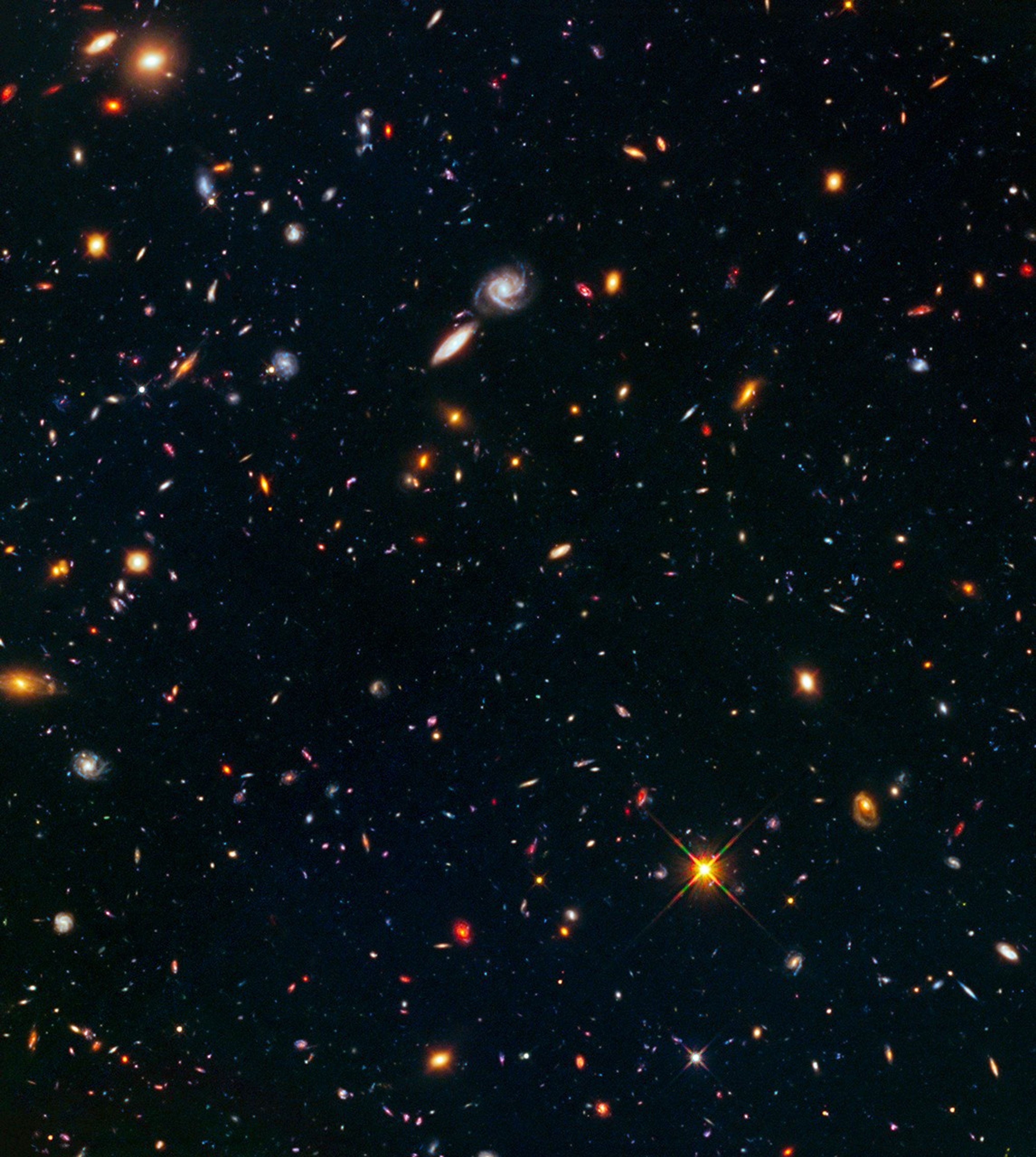 Hundreds of galaxies in a diverse array of shapes and colors are scattered across the dark background of space.